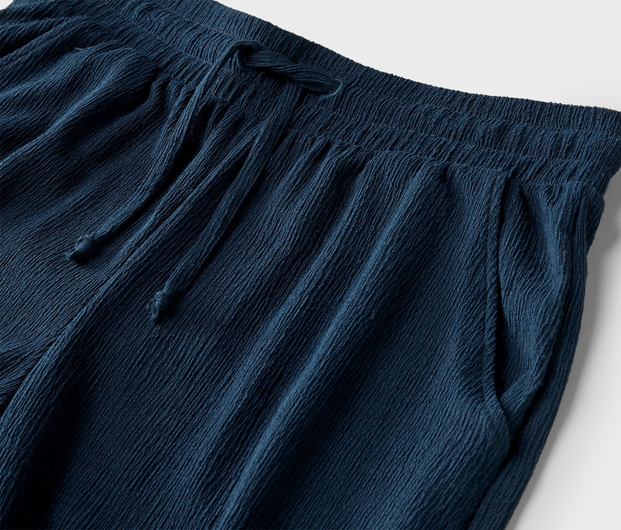Gros plan d'un pantalon bleu marine avec cordon de serrage et poches sur fond blanc.
