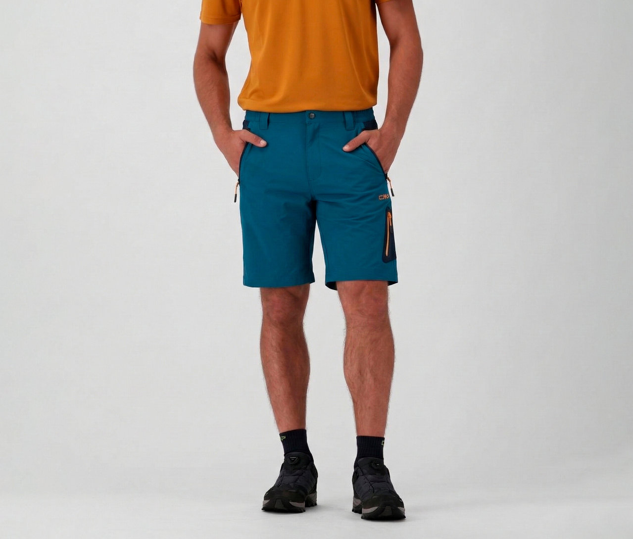 Homme portant un t-shirt orange et un bermuda stretch 4 directions CMP pour homme de couleur pétrole, les mains dans les poches.
