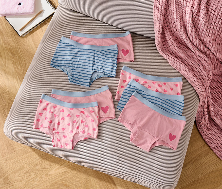 Six slips pour filles roses et bleus sont disposés sur un coussin rayé.