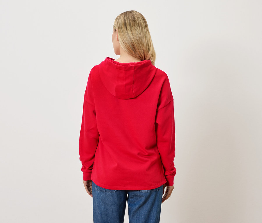 Vue arrière d'une femme blonde portant un sweat à capuche rouge et un jean.