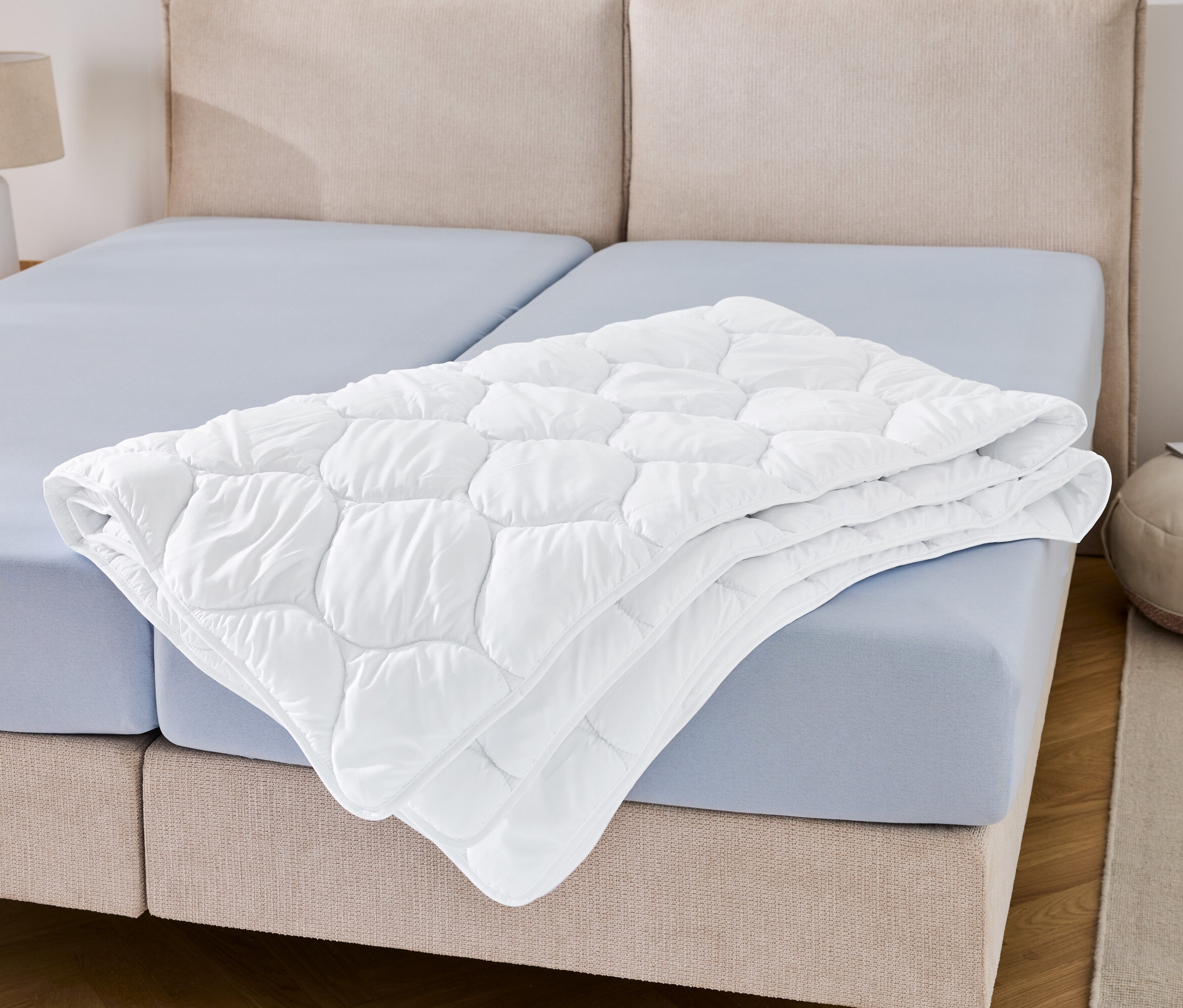 Une couette lavable à haute température, grande taille, est posée pliée sur un drap bleu.