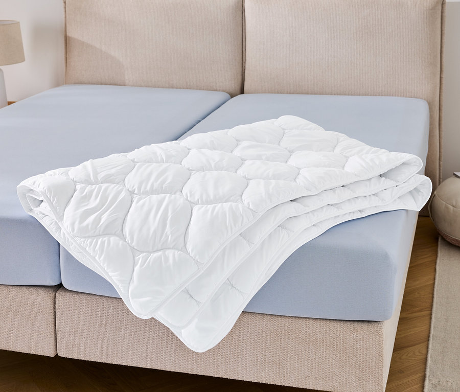 Une couette lavable à haute température, grande taille, est posée pliée sur un drap bleu.