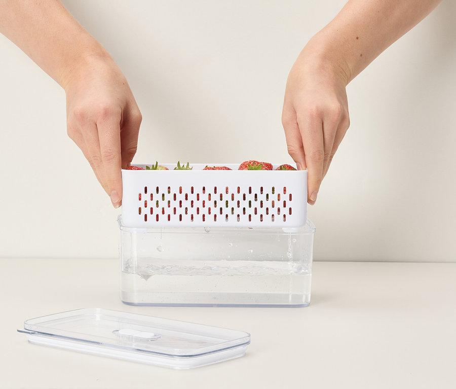 Des mains placent un récipient blanc rempli de fraises sur un récipient transparent rempli d'eau.