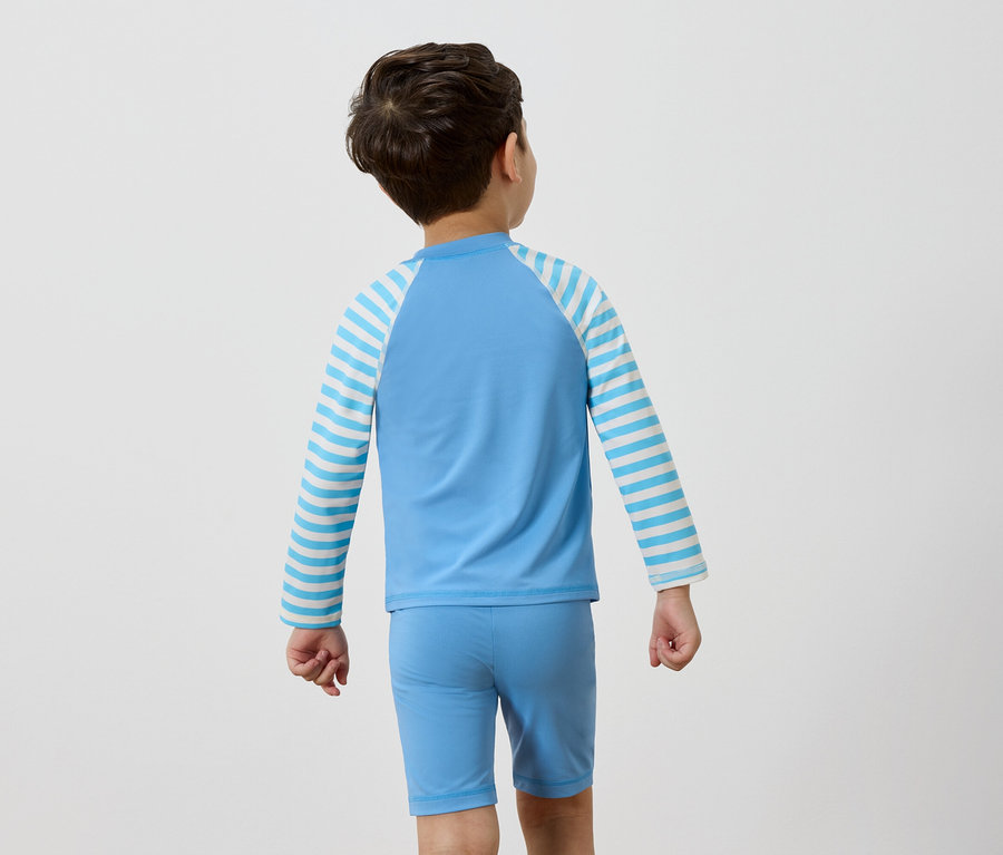 Vue arrière d'un garçon portant un haut de bain bleu clair avec des manches rayées bleu et blanc et un slip de bain assorti.