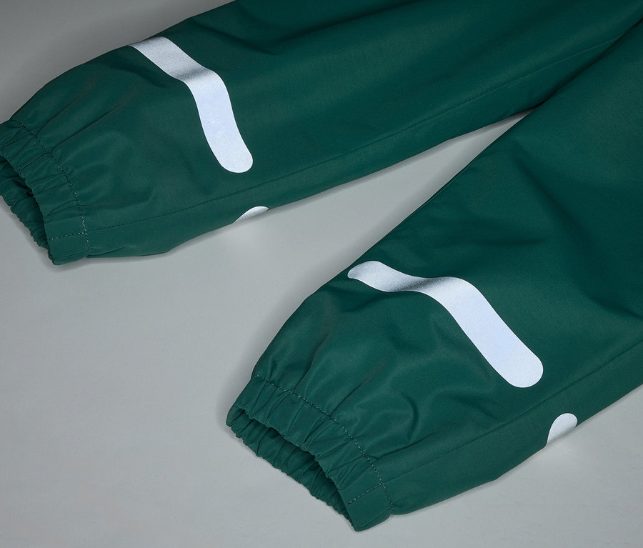Gros plan d'un pantalon de pluie vert avec des poignets élastiques et des bandes blanches réfléchissantes et incurvées sur un fond gris.