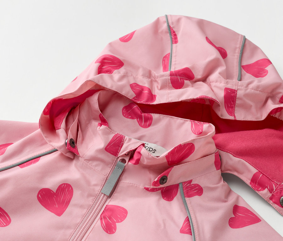 Gros plan sur un manteau pour enfant rose clair à capuche avec un motif de cœurs rose foncé.