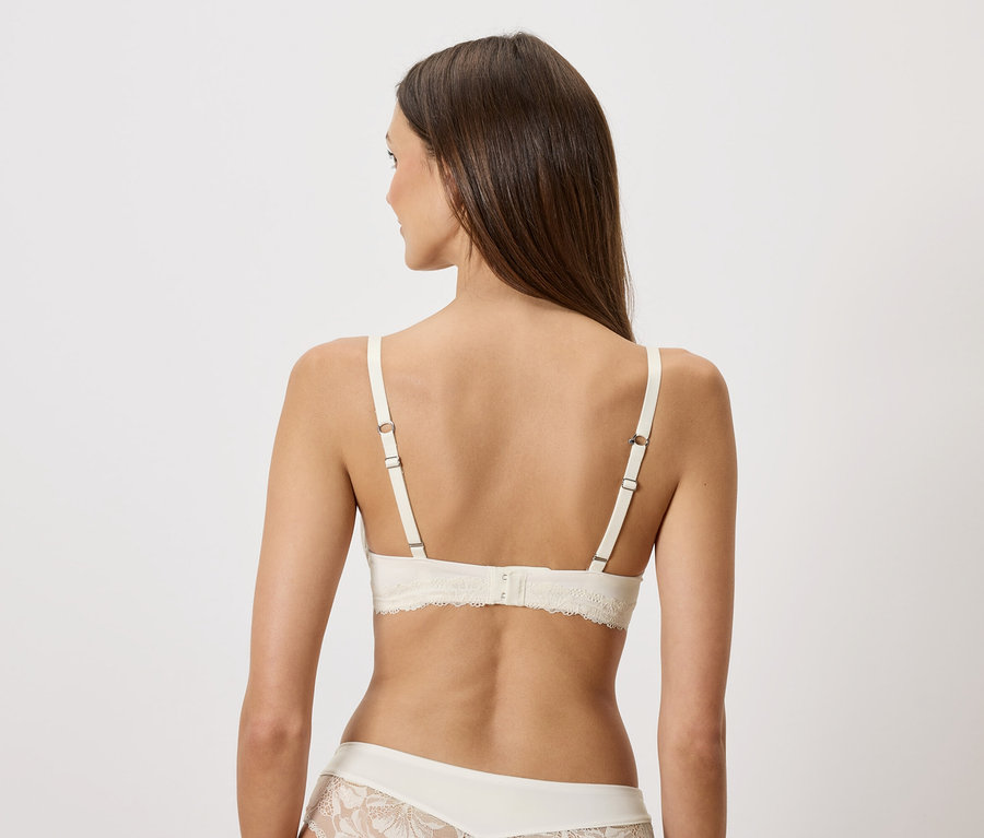 Vue arrière d'une femme aux longs cheveux bruns portant un soutien-gorge en dentelle crème et des sous-vêtements assortis.