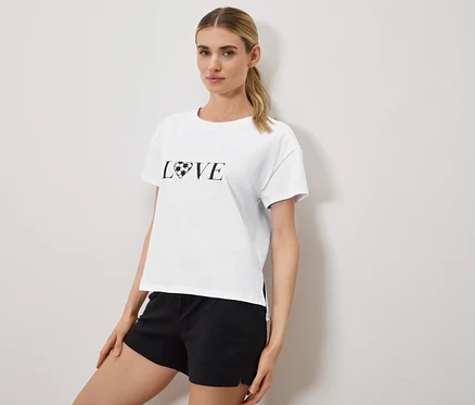 Femme portant un t-shirt blanc avec l'inscription "LOVE", le O étant remplacé par un ballon de football en forme de cœur, et un short noir.