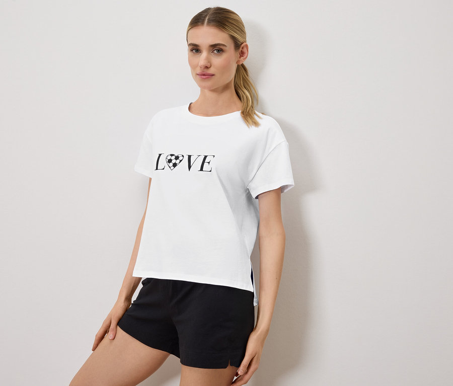 Femme portant un t-shirt blanc avec l'inscription "LOVE", le O étant remplacé par un ballon de football en forme de cœur, et un short noir.