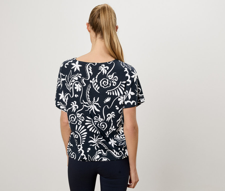 Vue de dos d'une femme avec une queue de cheval blonde portant un t-shirt bleu marine avec un motif floral blanc et un pantalon bleu marine.