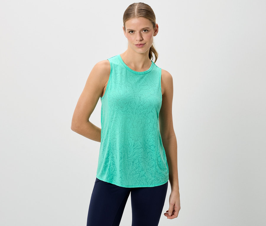 Une femme porte un débardeur vert et un legging bleu sur un fond blanc.