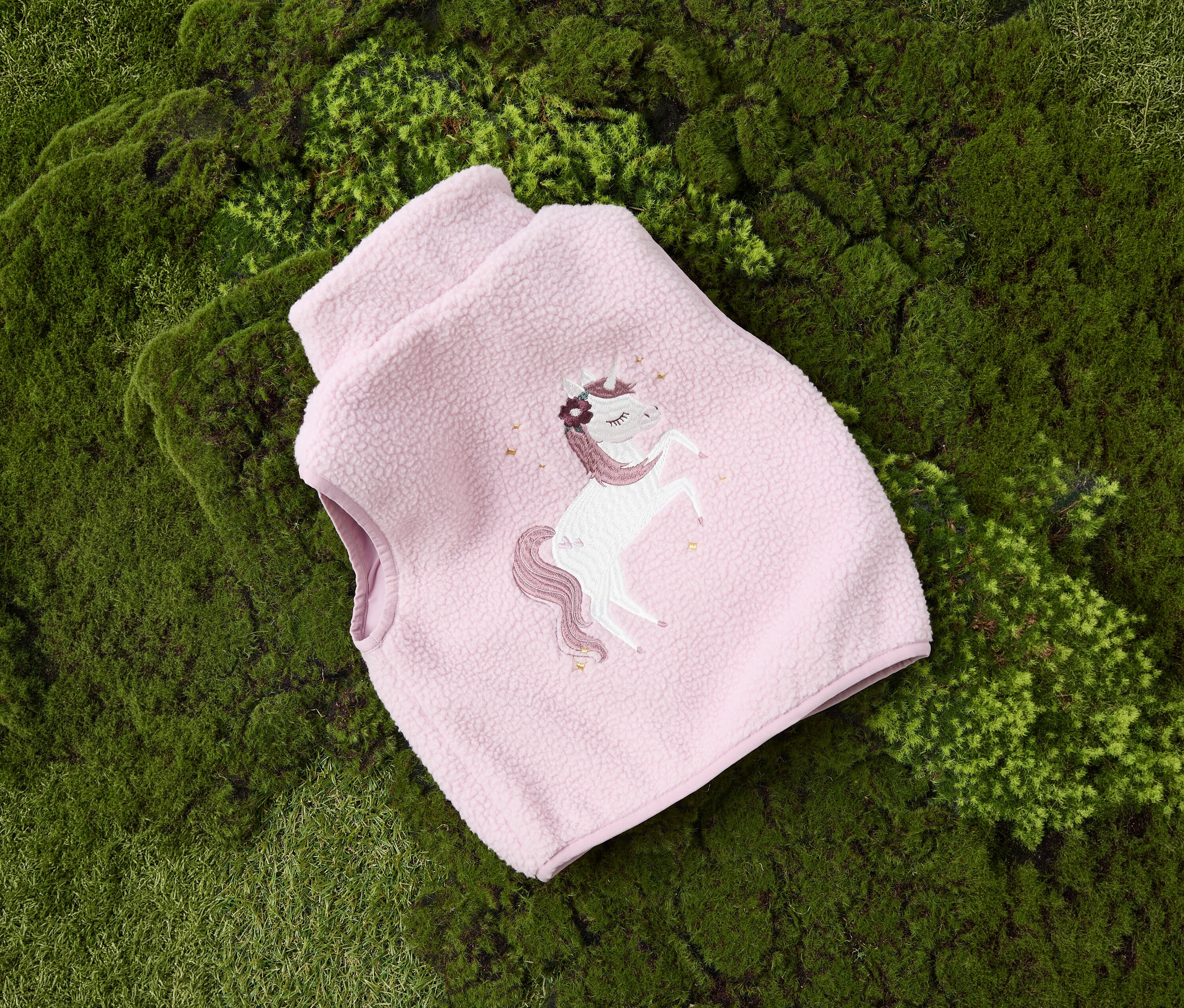 Un gilet en teddy pour enfant NAME IT rose avec une licorne sur de la mousse.