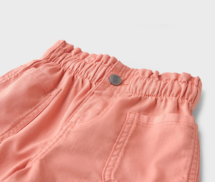 Gros plan d'un pantalon corail avec une taille élastique et un bouton.