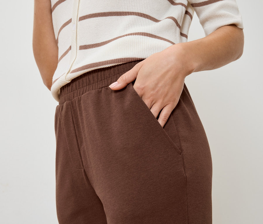 Gros plan d'une personne avec une main dans la poche d'un pantalon de jogging marron, avec un haut rayé assorti.