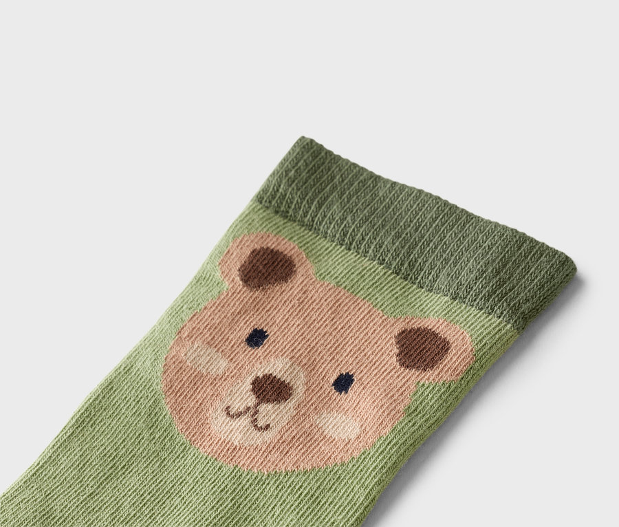 Gros plan d'une chaussette vert clair avec un visage d'ours dans les tons marron et rose.