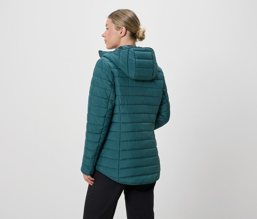 Une femme vue de dos, avec un chignon, porte une veste matelassée turquoise à capuche et un pantalon noir sur fond blanc.
