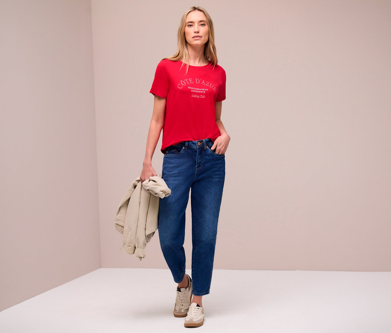 Une femme portant un jean et un t-shirt rouge Street One avec un imprimé, tenant une veste à la main.