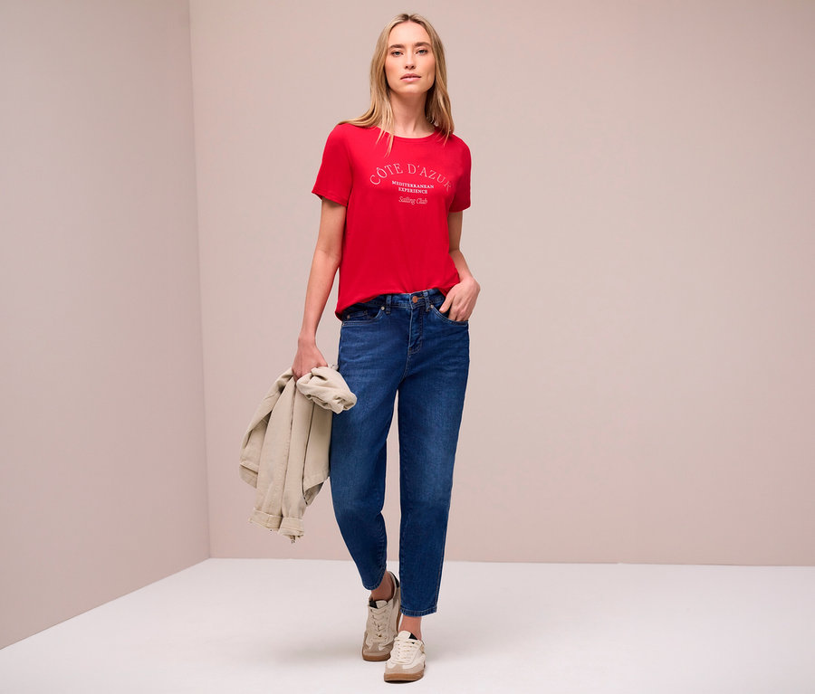 Une femme portant un jean et un t-shirt rouge Street One avec un imprimé, tenant une veste à la main.