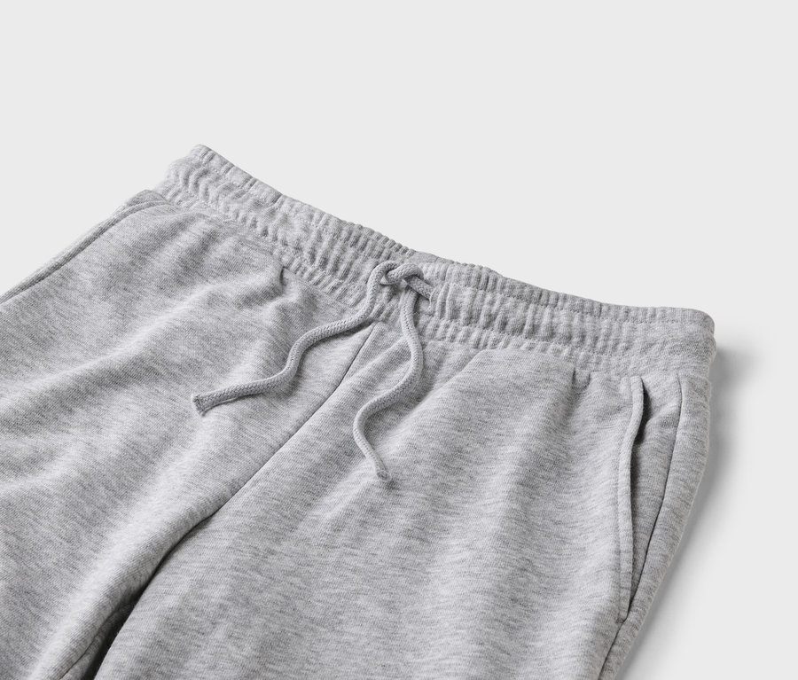 Gros plan d'un pantalon de jogging gris avec cordon de serrage et poches sur fond gris clair.