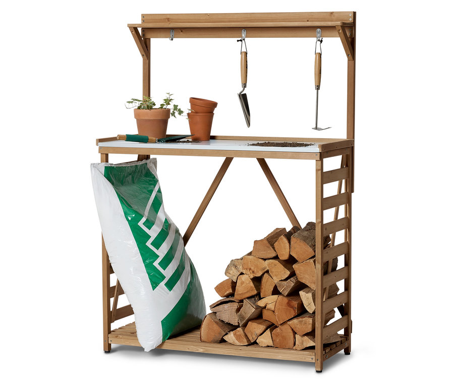 Une table de jardin en bois avec des pots de fleurs, des outils, un sac de terre et des bûches.