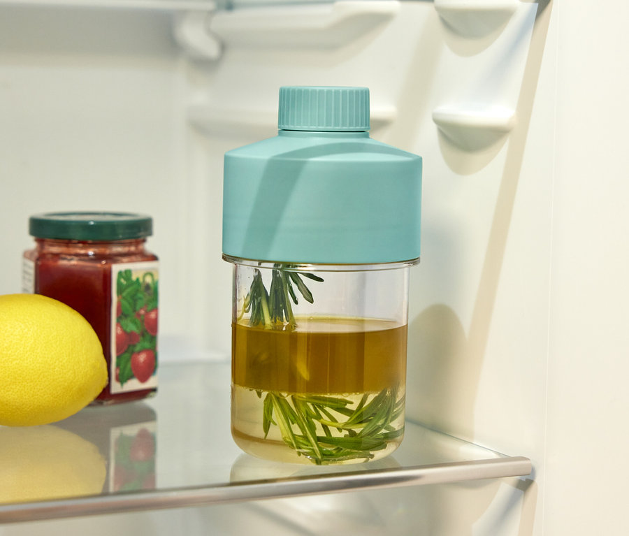 Sur une étagère en verre dans le réfrigérateur se trouvent un citron, un pot de confiture de fraises et un pot d'herbes dans de l'huile.