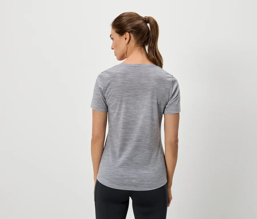 Vue de dos d'une femme avec une queue de cheval portant un t-shirt gris et un pantalon foncé sur un fond clair.