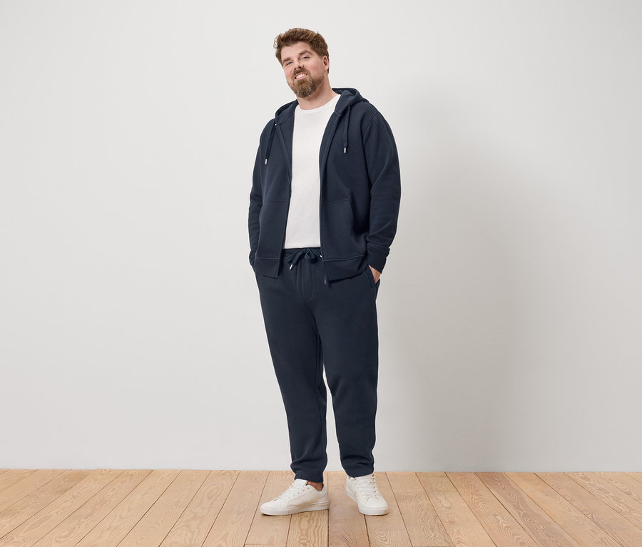 Homme debout en survêtement bleu marine et baskets blanches.