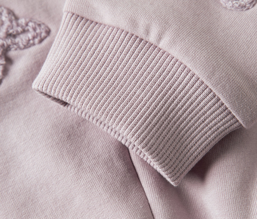 Gros plan sur la manche d'un sweat-shirt violet avec poignet côtelé et application florale.