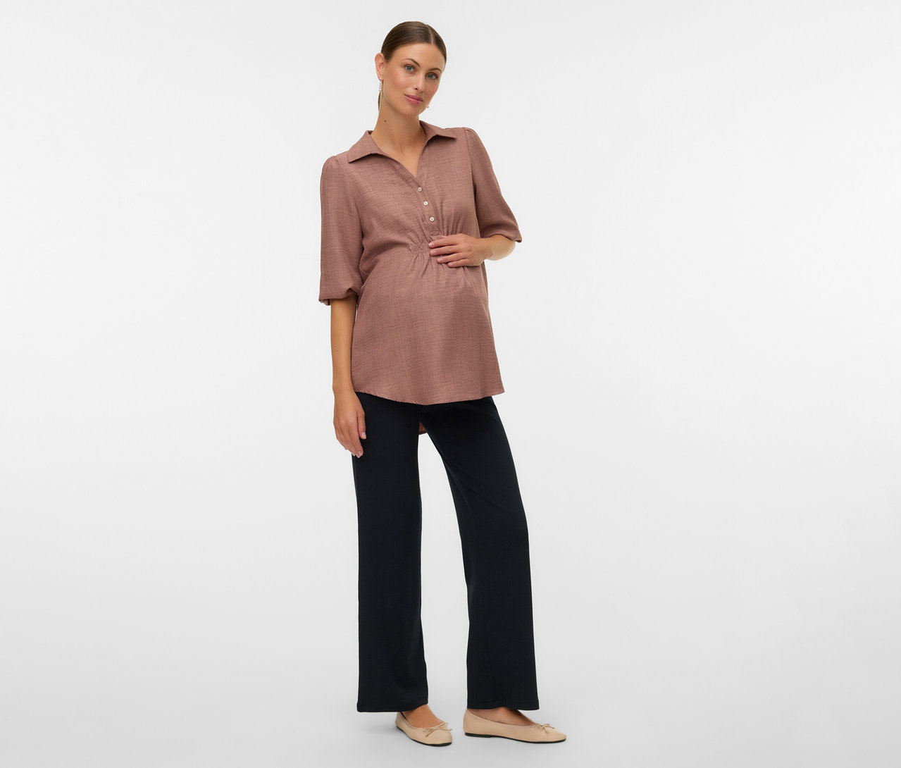 Femme enceinte avec chemisier marron et leggings décontractés MAMALICIOUS «
MLEMILY » posant sur fond blanc.