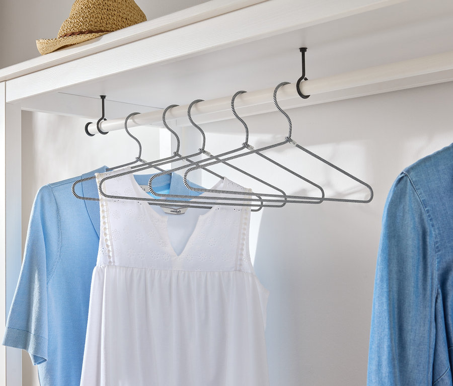 Des vêtements sont suspendus à des cintres dans une armoire blanche.