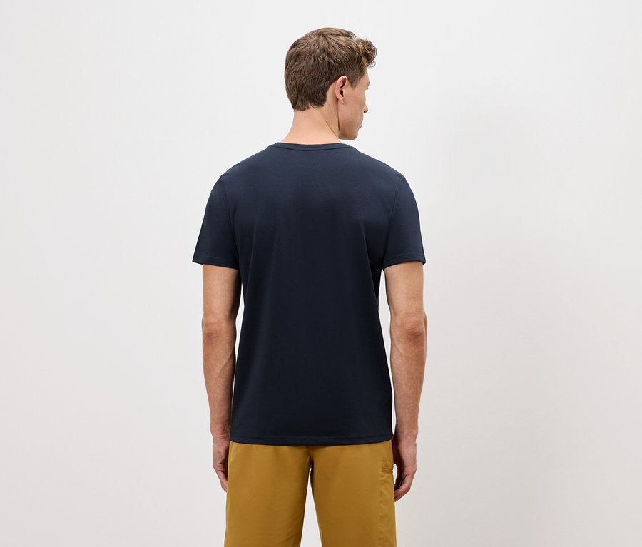 Un homme vu de dos portant un t-shirt bleu marine et un short doré sur un fond uni.