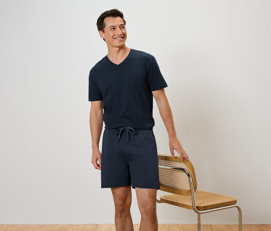 Un homme se tient à côté d'une chaise, portant un t-shirt et un short bleu marine.