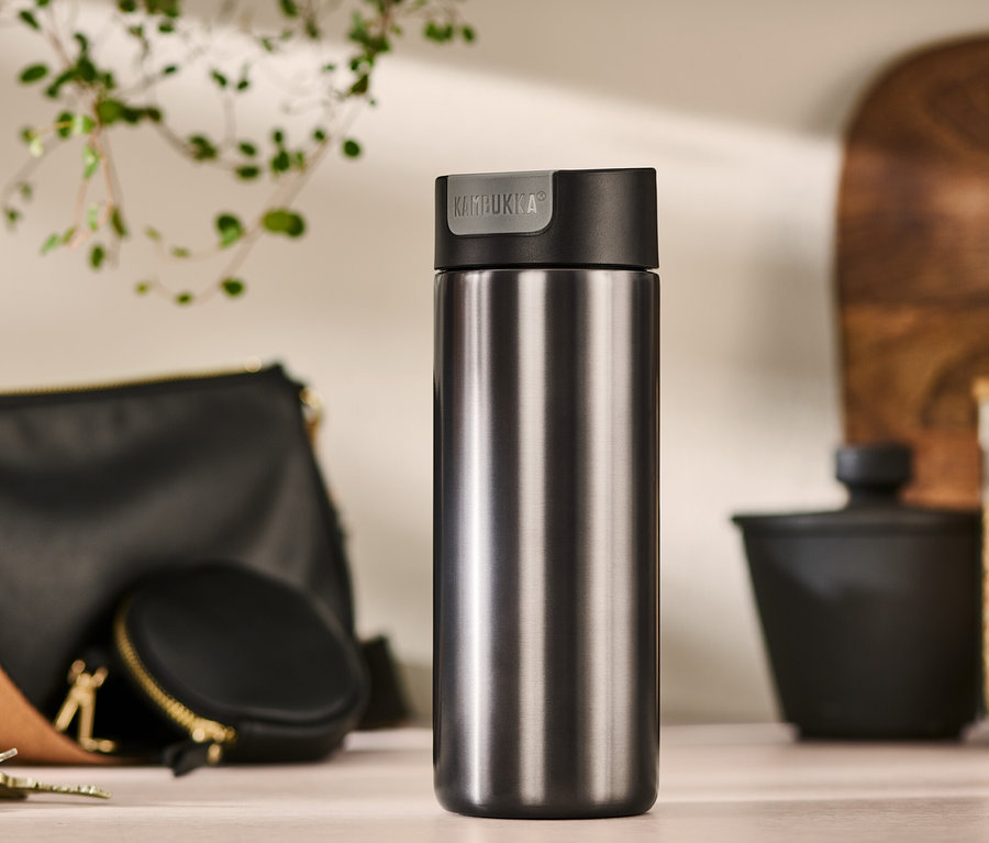 Un gobelet to-go Kambukka gris de 500 ml est posé sur une table à côté d'un sac à main, d'un porte-monnaie et de clés.