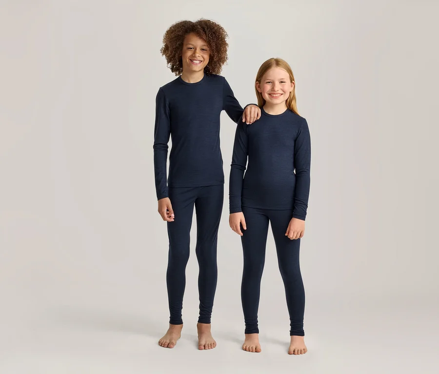Deux enfants souriants, un garçon aux cheveux bruns bouclés et une fille aux cheveux blonds raides, se tiennent côte à côte dans des t-shirts à manches longues et des leggings bleu marine assortis. Le garçon plus grand a son bras sur l'épaule de la fille; tous deux sont pieds nus.