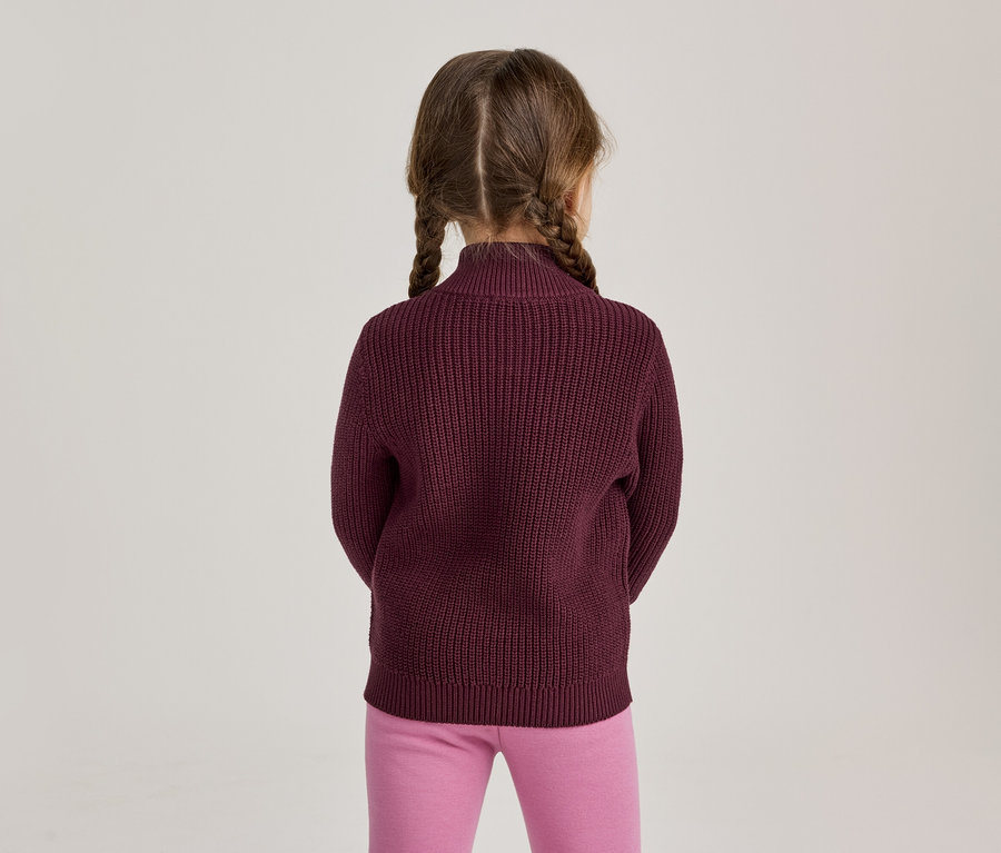 Jeune fille vue de dos, portant un pull en tricot bordeaux et un legging rose, avec ses cheveux tressés en deux nattes.