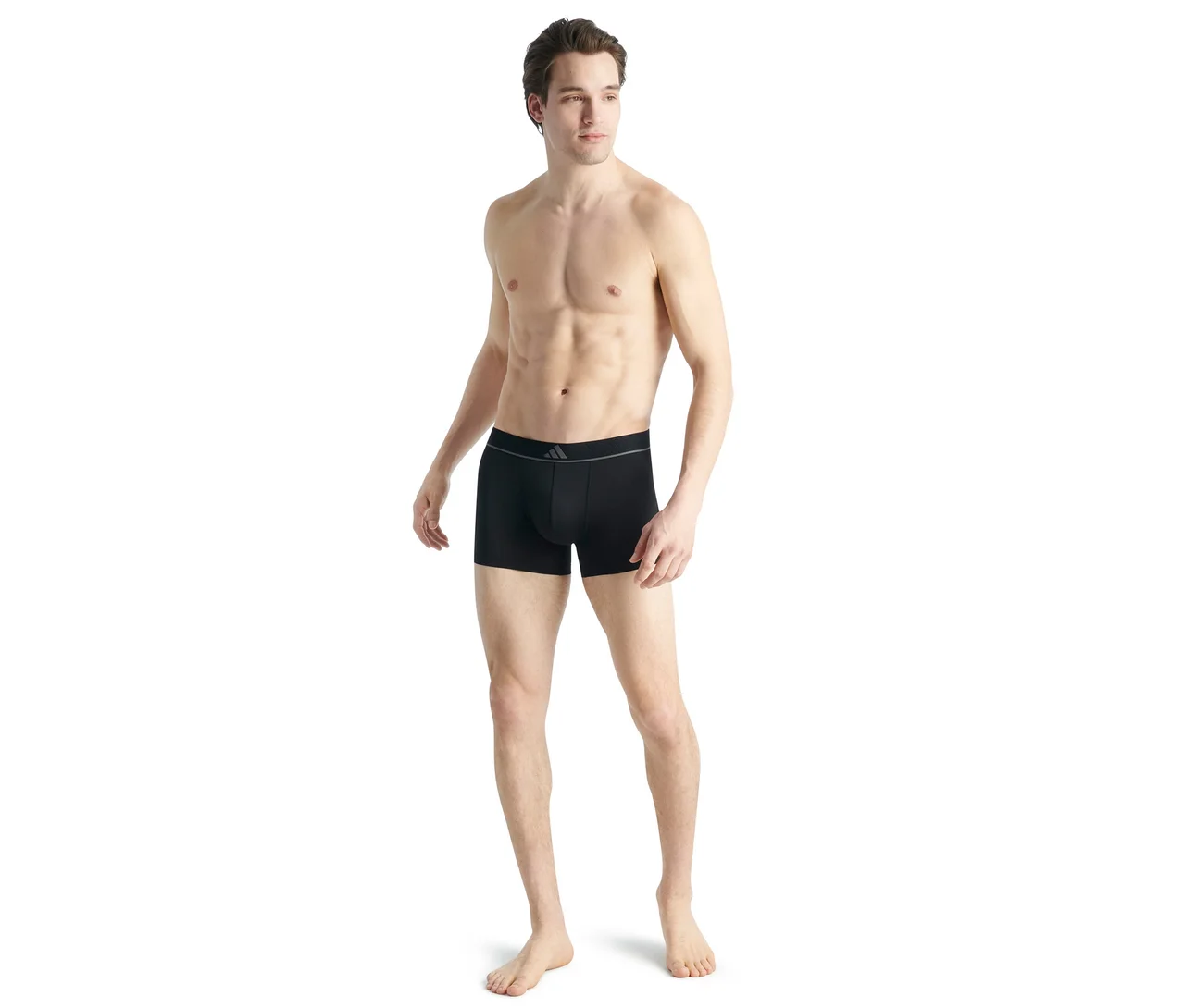 Un homme torse nu à la silhouette athlétique porte un boxer noir avec une ceinture grise et un petit logo, debout et regardant vers la droite.