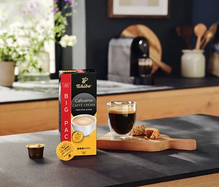 Paquet de Cafissimo Caffè Crema mild (doux) – 30 capsules, une tasse de café et une machine à café sur un plan de travail de cuisine.
