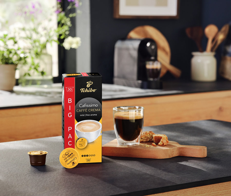 Paquet de Cafissimo Caffè Crema mild (doux) – 30 capsules, une tasse de café et une machine à café sur un plan de travail de cuisine.