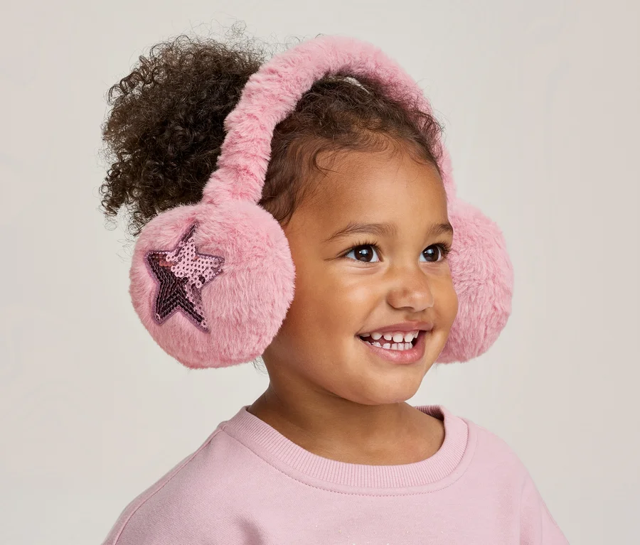 Enfant souriant aux cheveux bouclés portant un cache-oreilles rose duveteux avec des étoiles à paillettes.