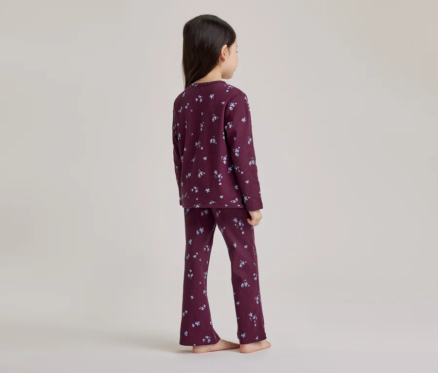 Jeune fille vue de dos, portant un pyjama côtelé violet foncé à motif floral clair, pieds nus.