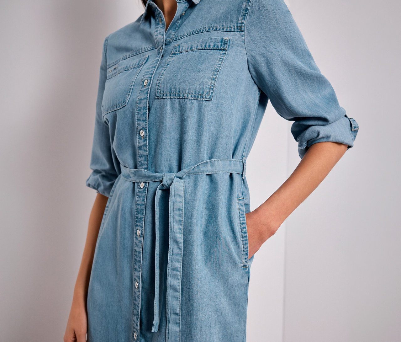 Personne portant une robe en jean Street One bleu clair avec ceinture à nouer et manches retroussées, une main dans la poche.
