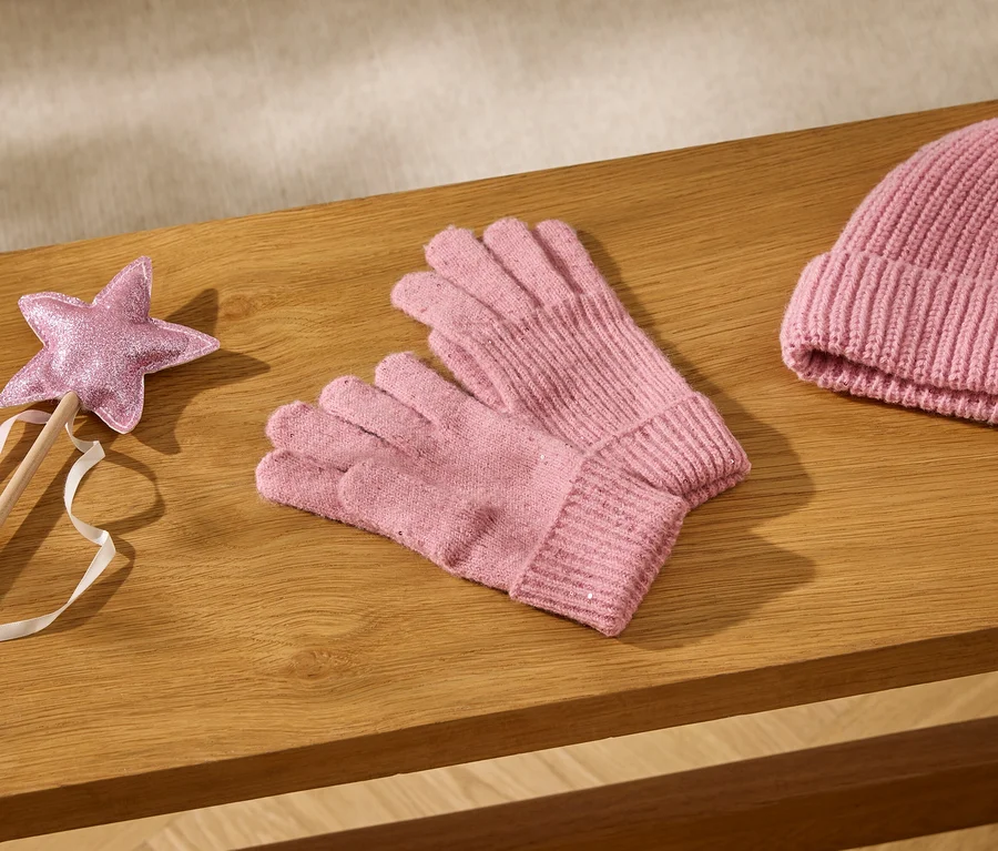Baguette étoile rose pailletée avec rubans, gants tricotés roses et bonnet tricoté rose posés sur une surface en bois.