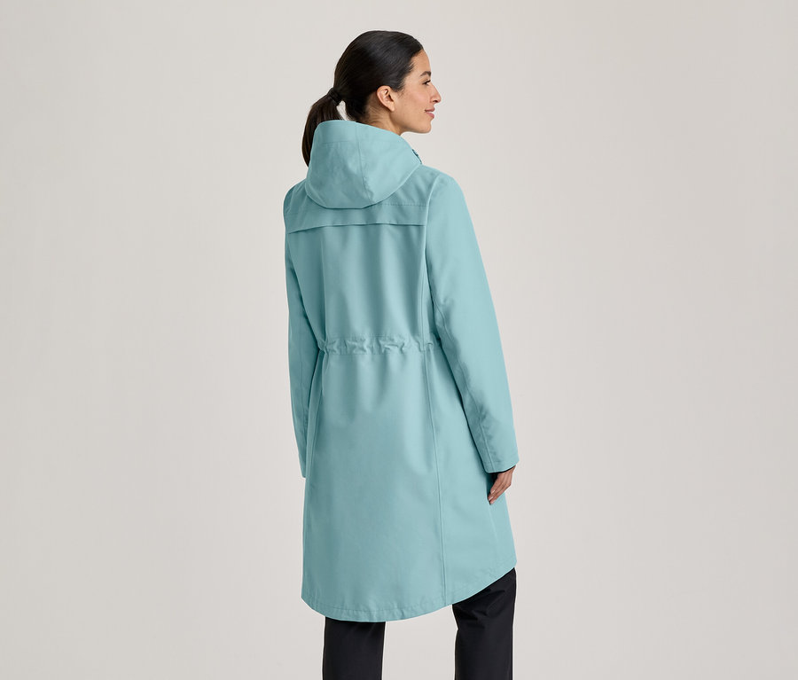 Femme de dos portant un long manteau turquoise clair avec capuche et cordon de serrage à la taille, regardant vers sa droite.