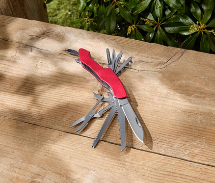 Un outil multifonction rouge est ouvert sur une surface en bois.