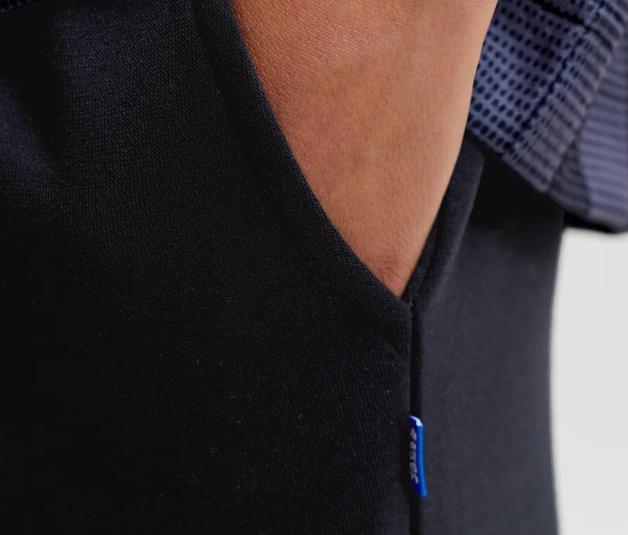 Gros plan d'une main dans la poche d'un pantalon de survêtement noir Jack&Jones Bradley, avec une étiquette bleue sur le côté.