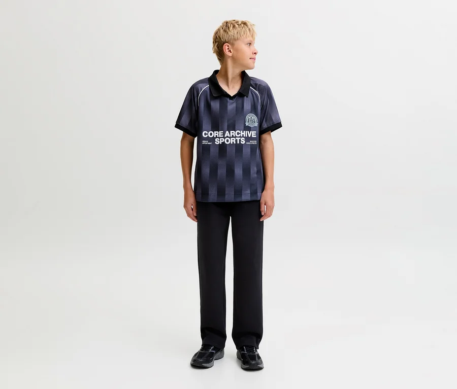 Jeune garçon portant un polo rayé foncé et un pantalon de survêtement noir Jack&Jones Bradley, debout et regardant vers la droite.