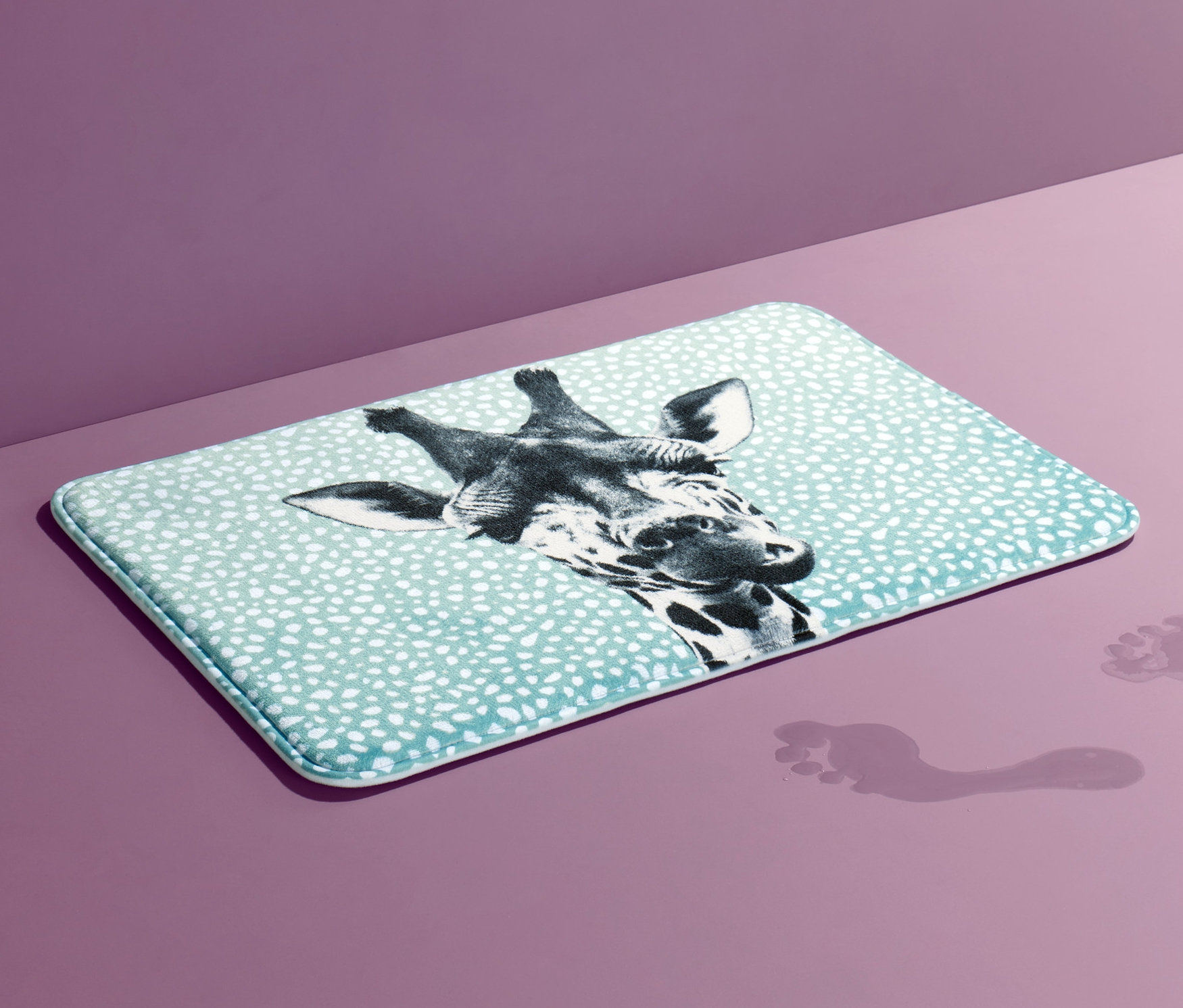 Un tapis de bain confort bleu clair avec un imprimé girafe et des empreintes de pas sur un fond violet.