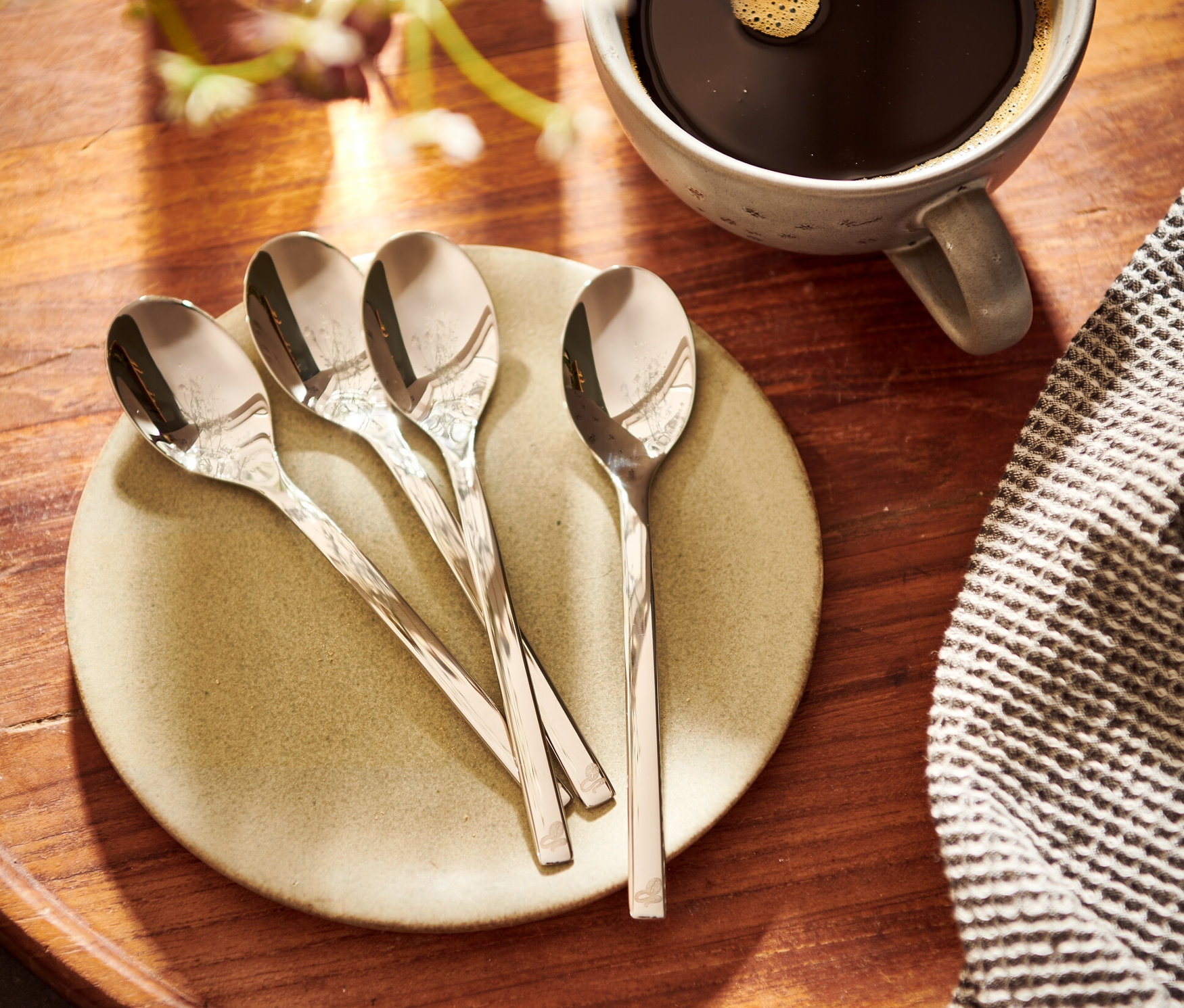 Quatre cuillères à café sur une assiette à côté d'une tasse de café.