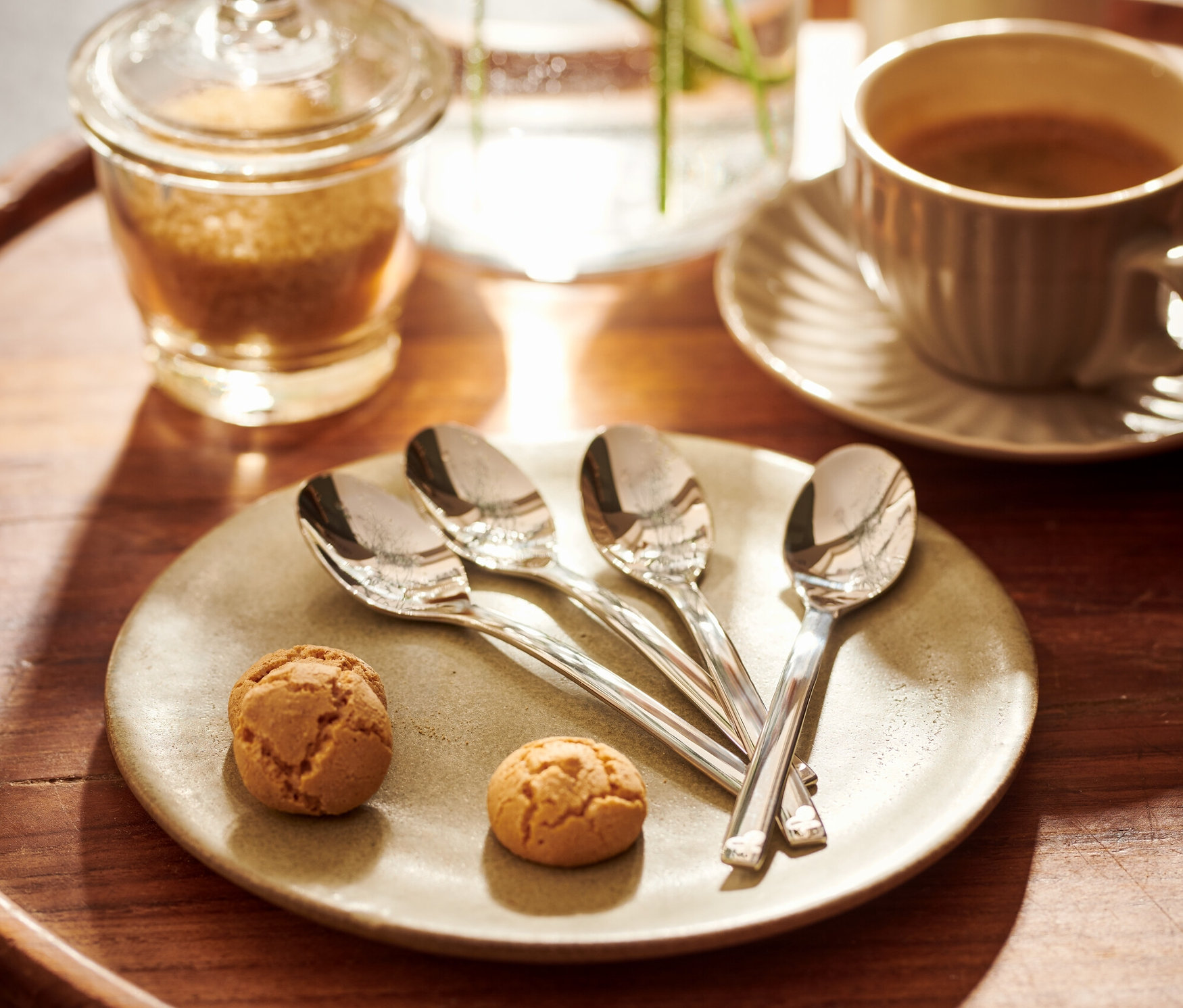 Sur un plateau en bois, 4 cuillères à expresso sont posées à côté de deux biscuits sur une assiette.