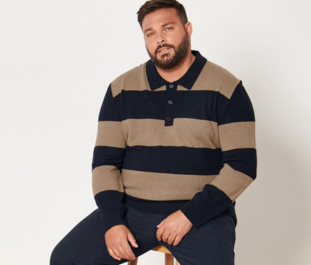 Un homme est assis sur un tabouret et porte un pantalon chino bleu foncé et un pull rayé avec du cachemire.